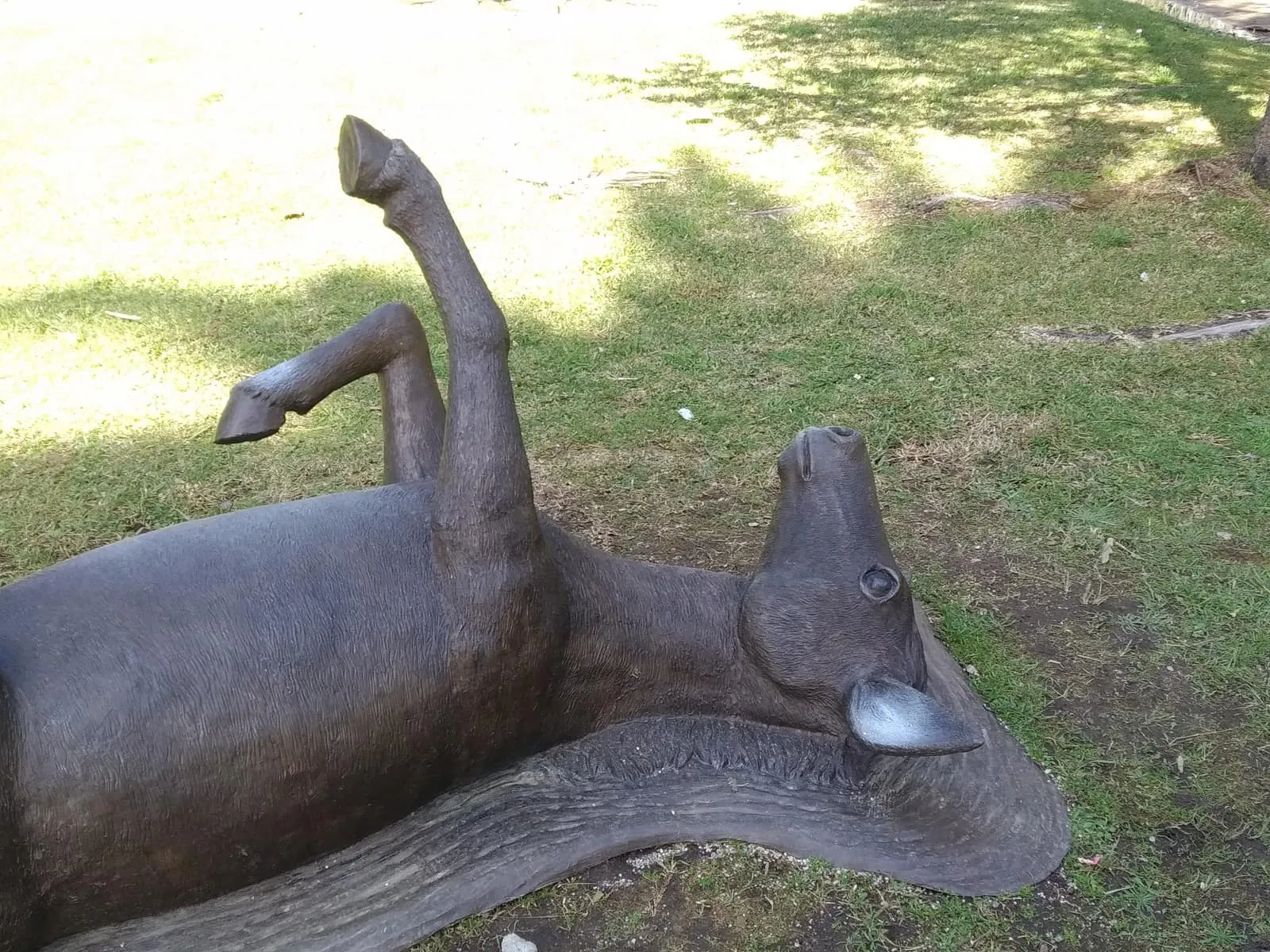 Escultura de bronce de un burro tumbado panza arriba, revolcándose, en un jardín de A Toxa