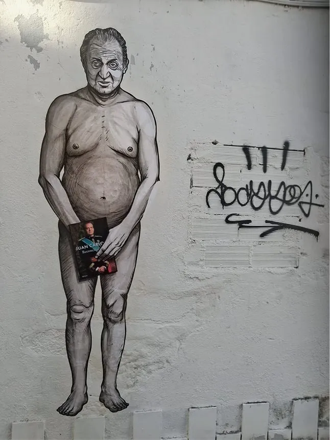 Detalle del grafiti «O traxe novo do rei» de Primo Banksy en la rúa das Reyes de Bouzas, con Juan Carlos I desnudo sujetando sus memorias
