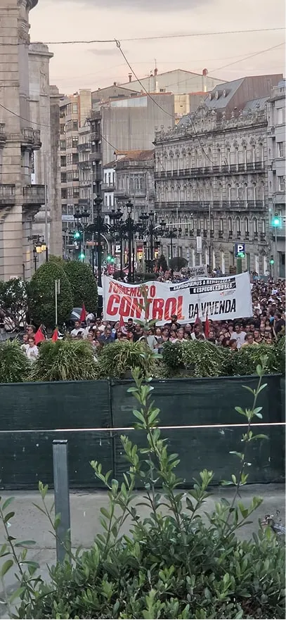 Pancarta «Tomemos o control da vivenda» sobre la multitud, en una calle del centro de Vigo