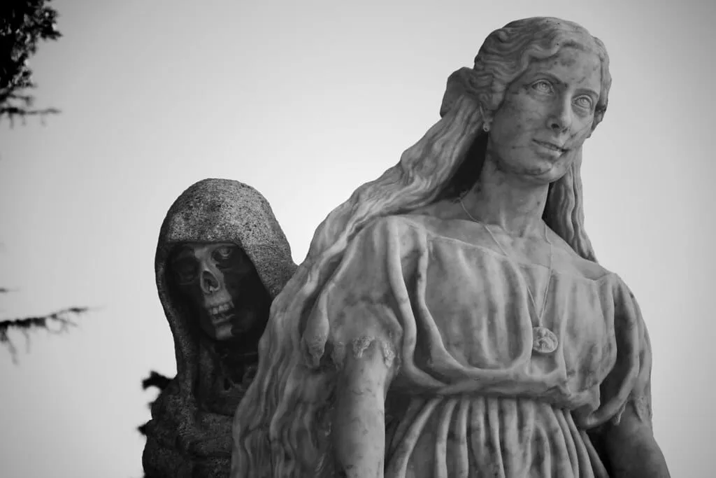 Escultura de mármol de una joven de pelo largo con la figura encapuchada de la Muerte, con rostro de calavera, a su espalda