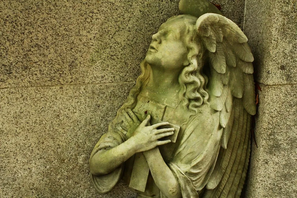 Relieve de un ángel de piedra con las manos sobre el pecho y la mirada hacia arriba