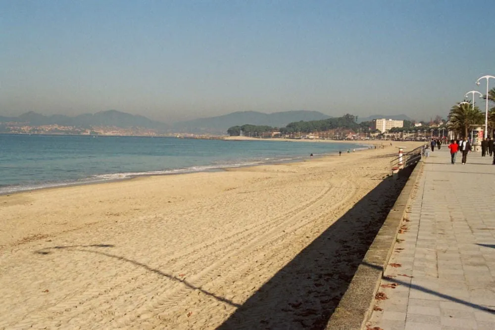 La playa de Samil con su paseo marítimo, palmeras y la costa del Morrazo al fondo