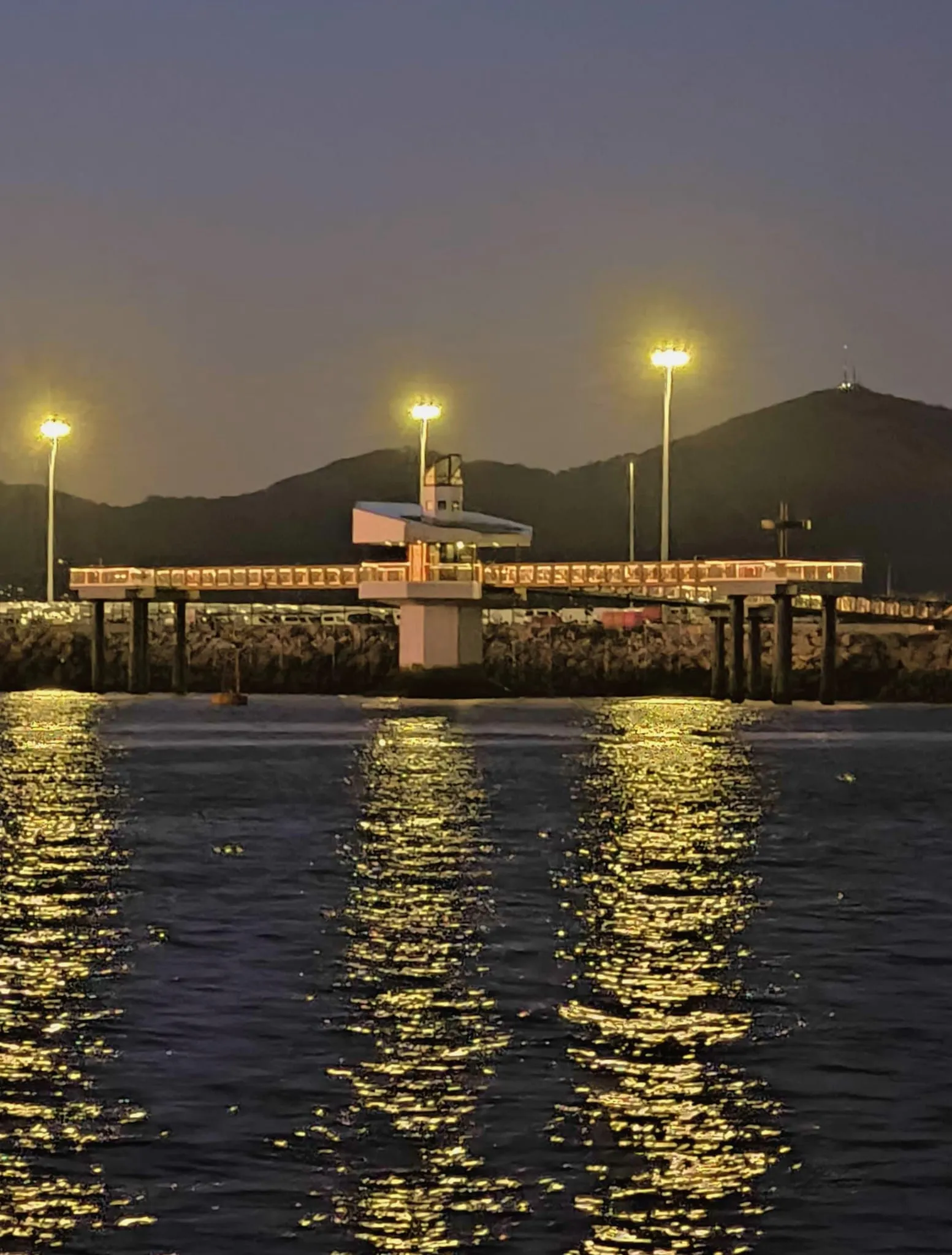 El visor submarino Atlántida, una pasarela elevada iluminada sobre la ría de Vigo al anochecer, junto a la terminal de vehículos de Bouzas