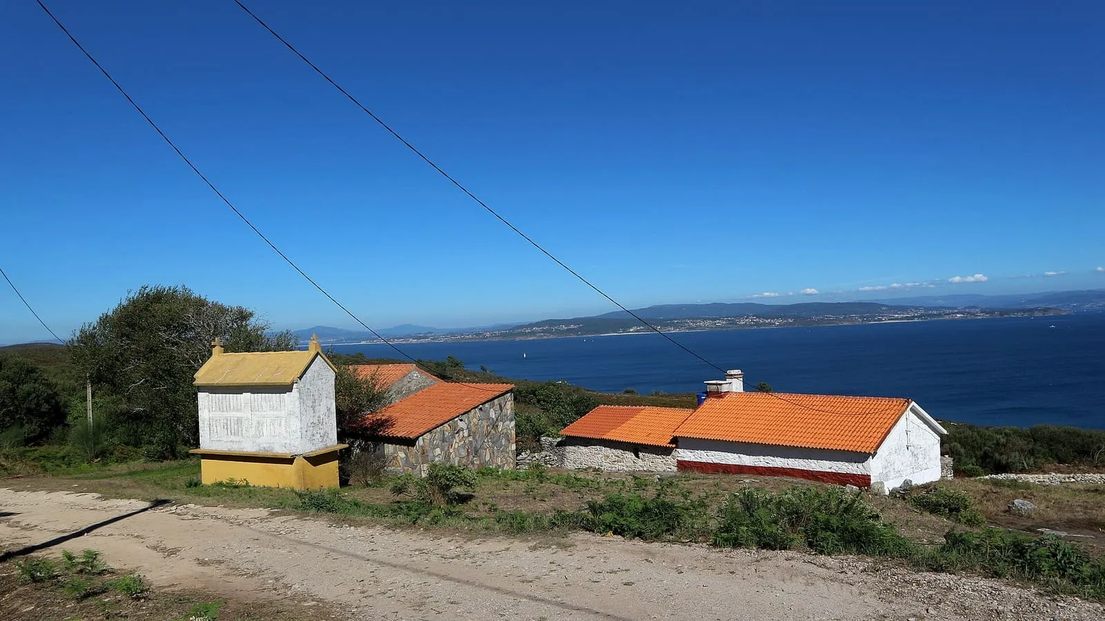 Casas tradicionales con tejados rojos junto a un camino de tierra en la isla de Ons, con la ría al fondo
