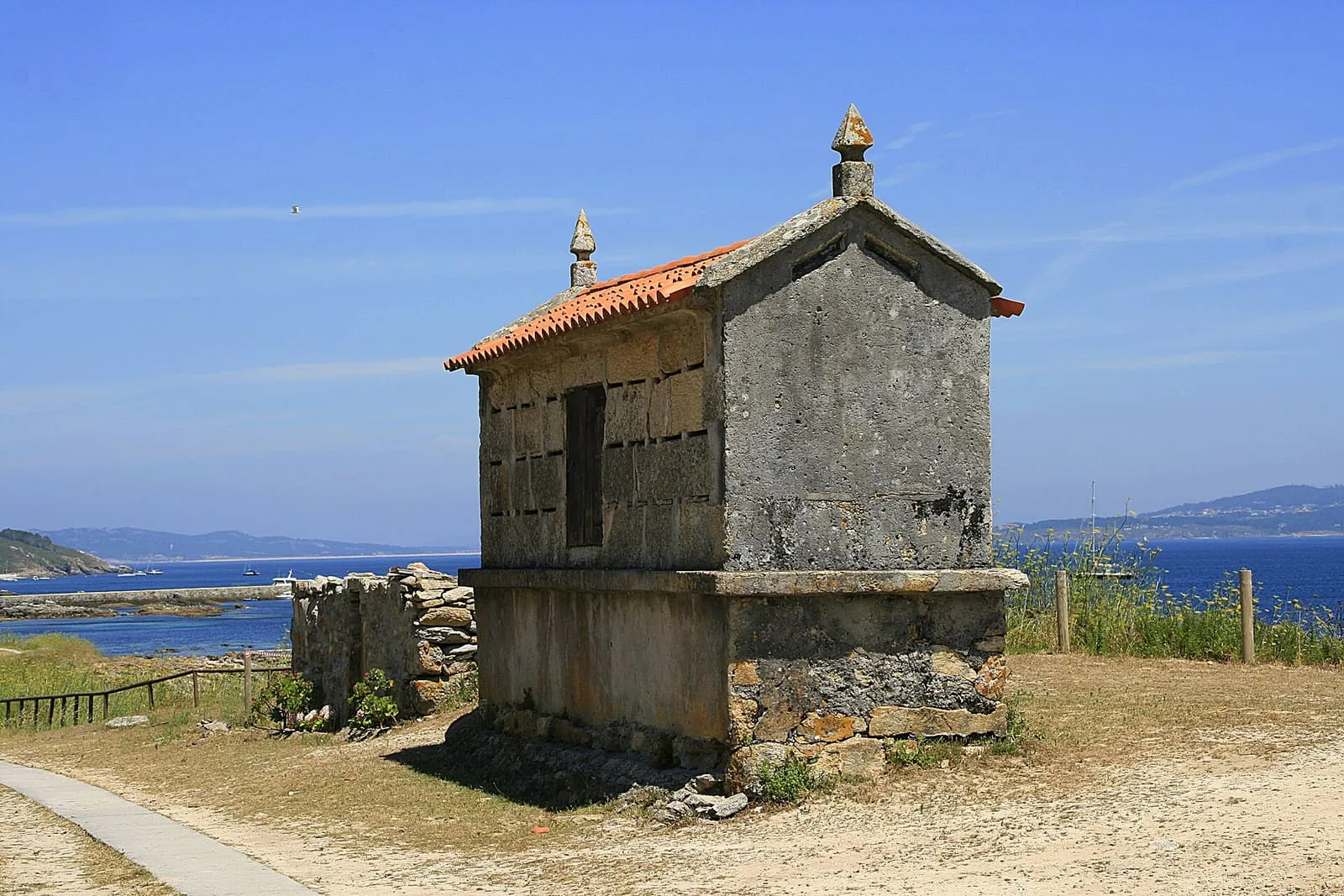 Hórreo de piedra con tejado de teja sobre un muro, con el mar de fondo, en la isla de Ons