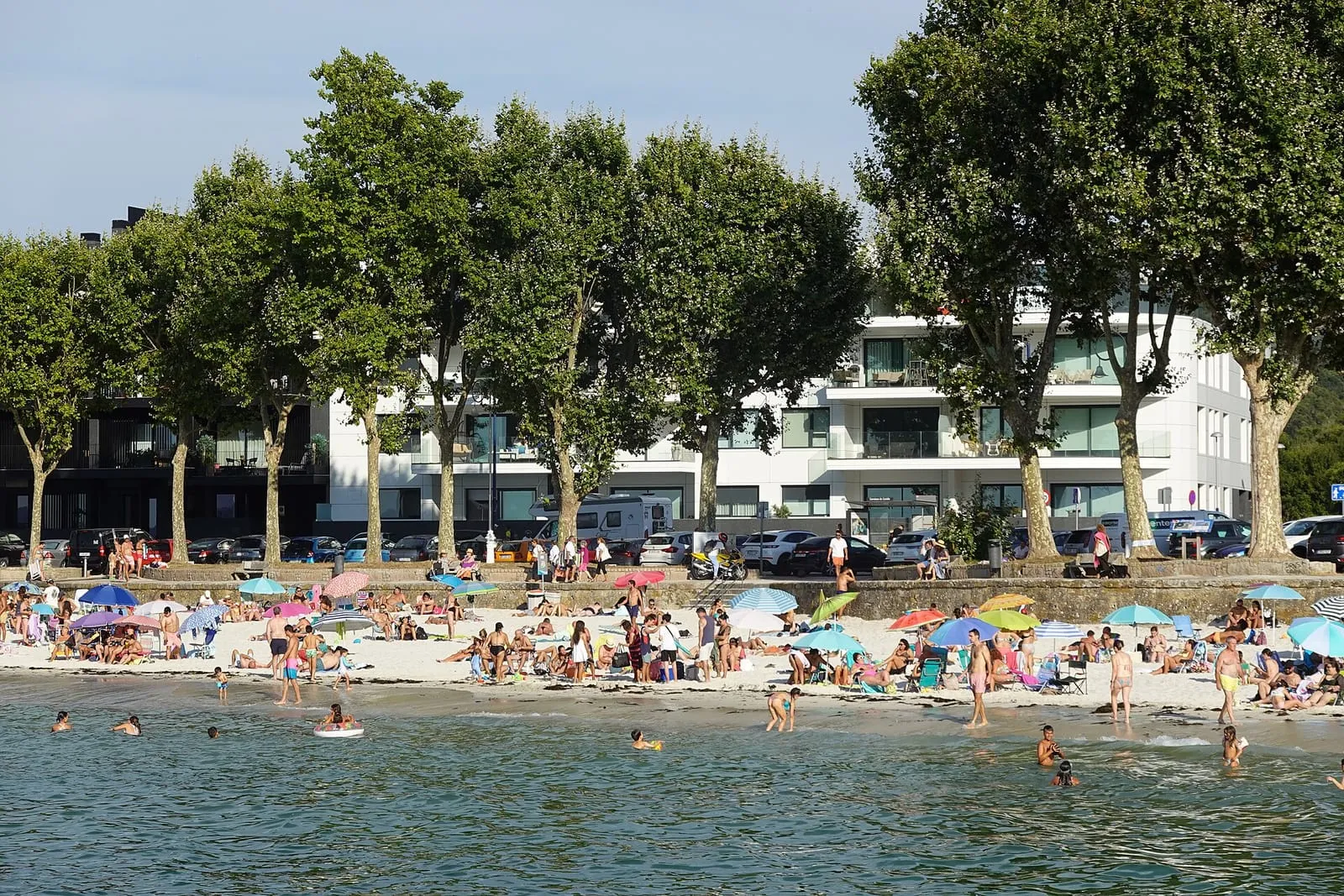 Bañistas y sombrillas en la playa de Canido, con los edificios del paseo detrás