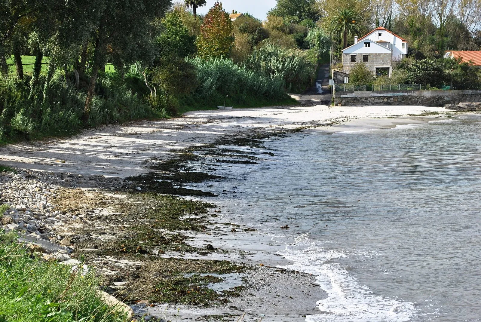 Orilla rocosa de la playa do Carril, en Alcabre, con casas al fondo