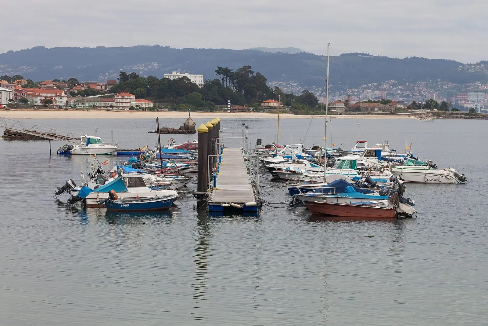 Embarcaciones amarradas en el puerto de Cangas con la playa al fondo